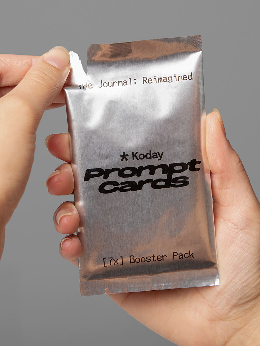 hand holding silver packaging of Koday Prompt Cards Booster Pack against a gray background
